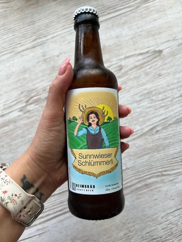 Hand hält eine Bierflasche mit individuell gestalteter Etikette „Sunnwieser Schlümmeri“ – Kundenauftrag von ArtKristy.